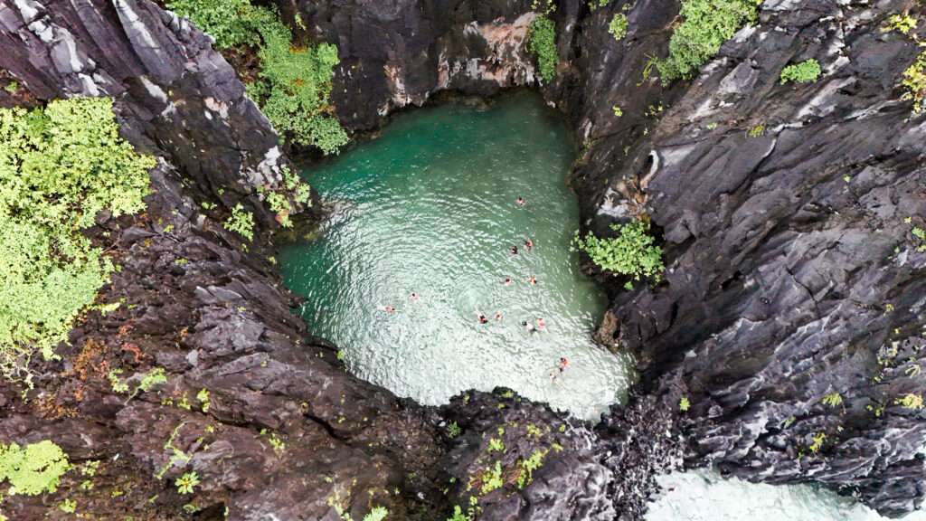 Swimmer entering Secret Lagoon through a narrow gap in the limestone rock