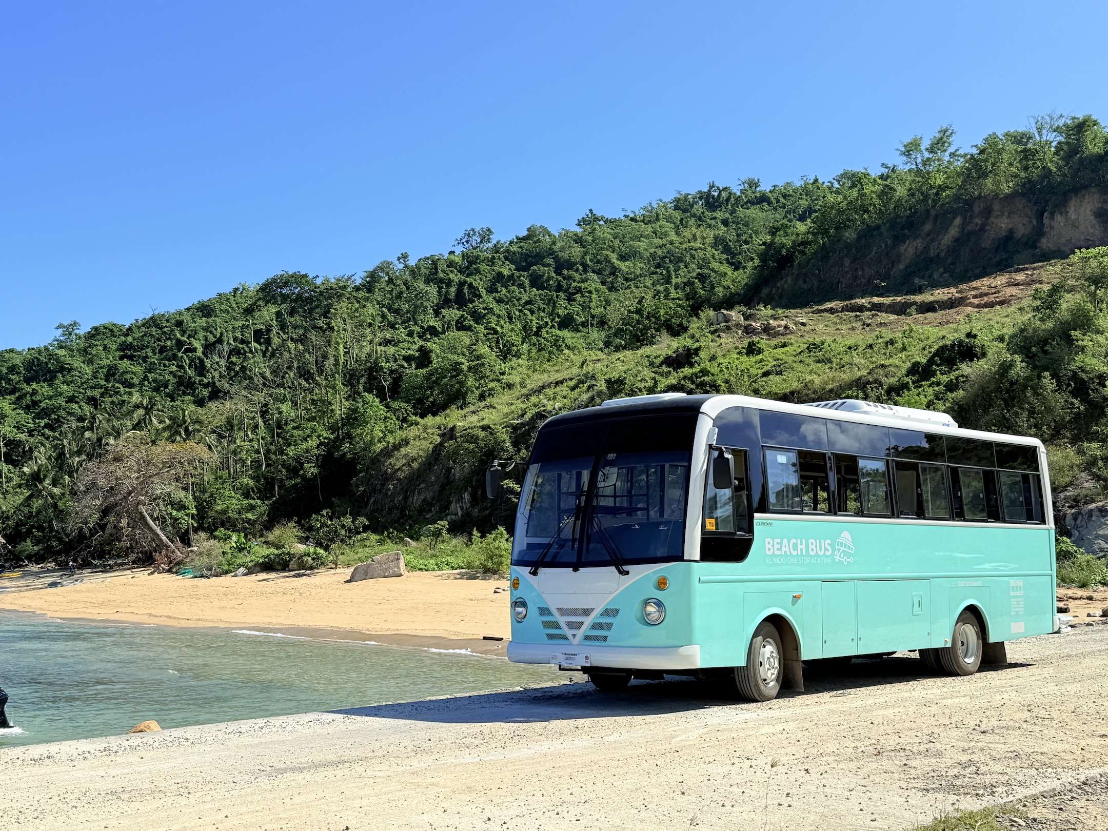 Turquoise El Nido Beach Bus hop-on hop-off coach parked beside the sand.